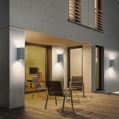 Modern outdoor seating area with chairs and a table on a wooden deck, illuminated by wall lights.
