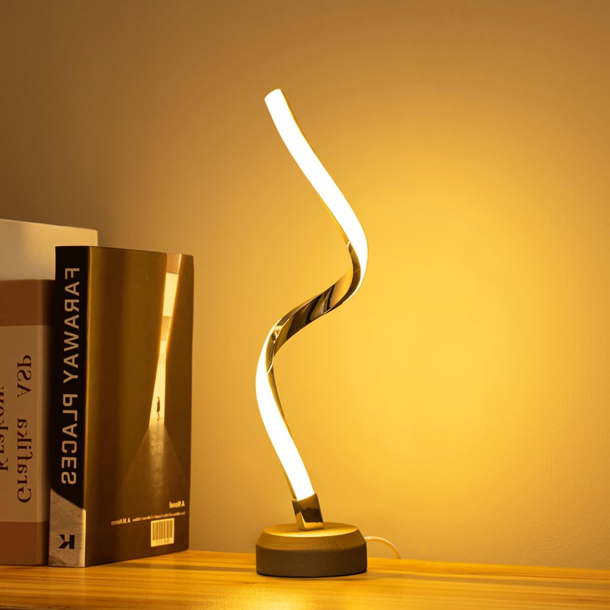 Modern table lamp with curved design on a wooden surface next to books, warm lighting.