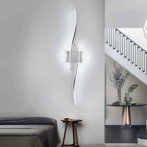 Modern wall-mounted light fixture in a bedroom setting with a bed and side table.