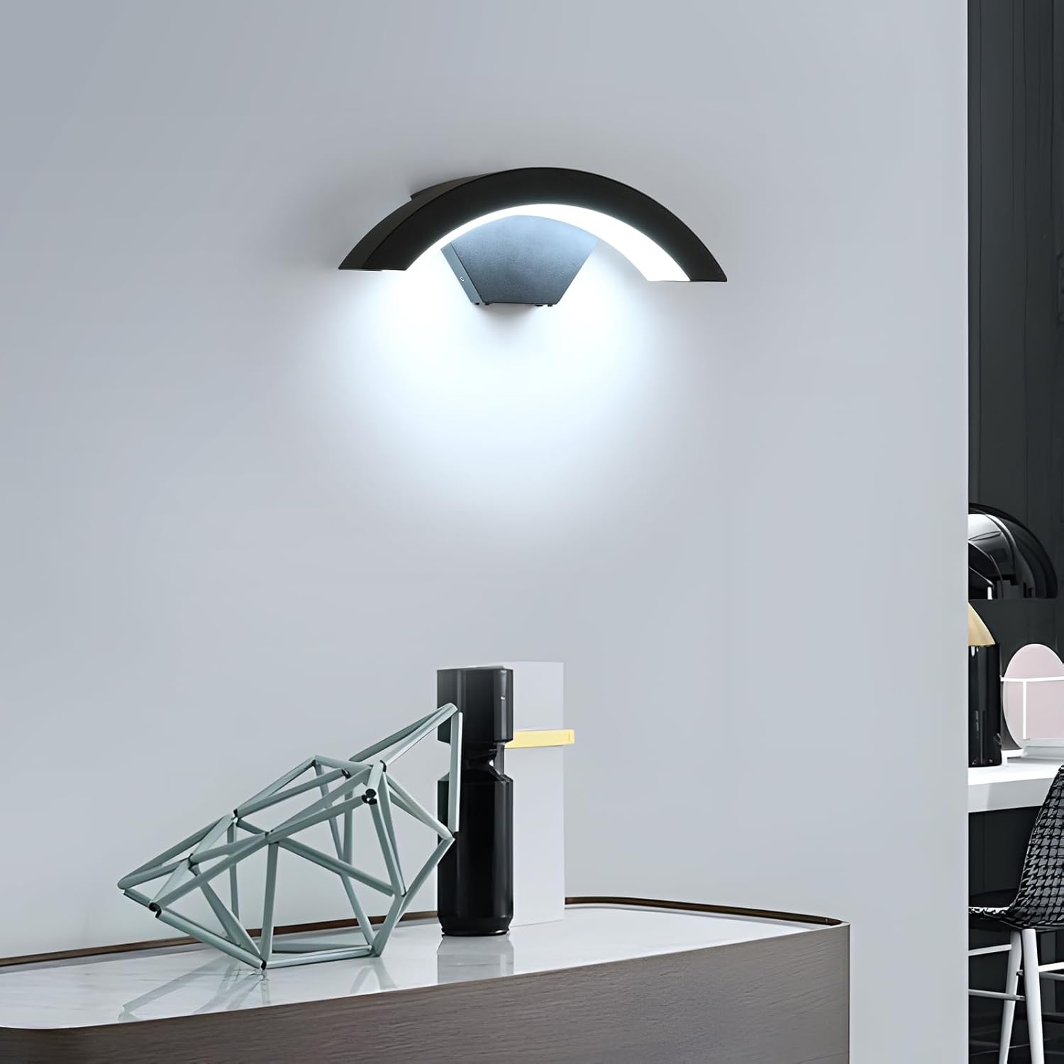 Modern wall-mounted light fixture on a white wall with a desk and chair in the foreground.