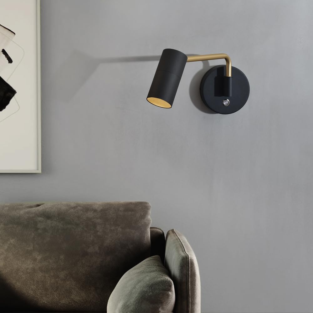 Modern wall lamp with black and gold design on a gray wall above a sofa.