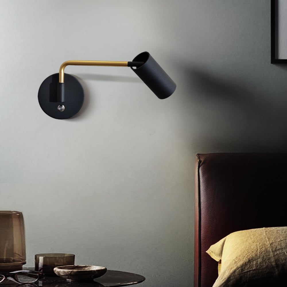 Modern wall lamp with black and gold design on a gray wall next to a bed.