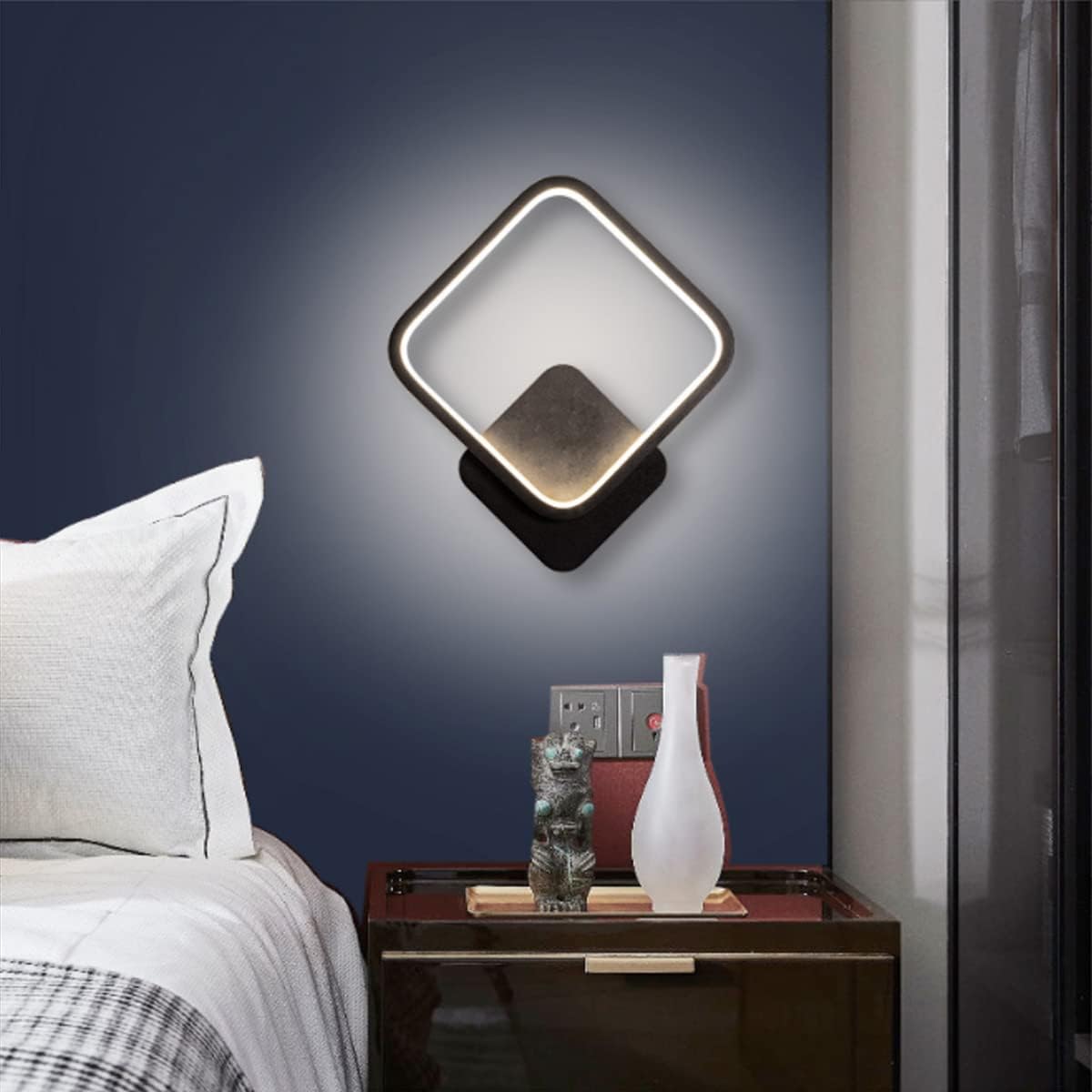 Modern wall sconce above a nightstand with decorative items in a bedroom setting.