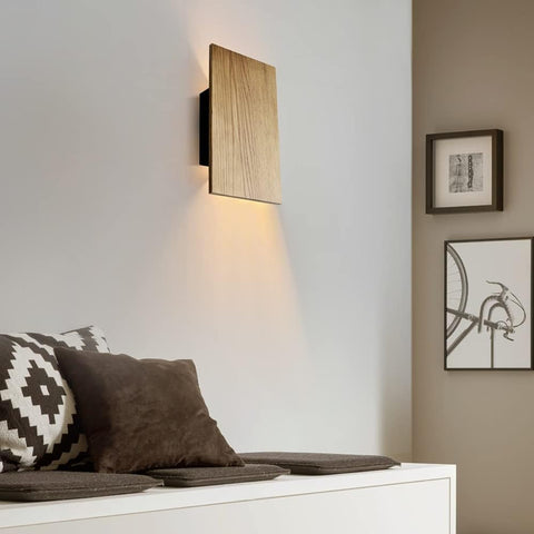 Modern wall sconce lighting fixture on a white wall with decorative pillows and framed art in the foreground.