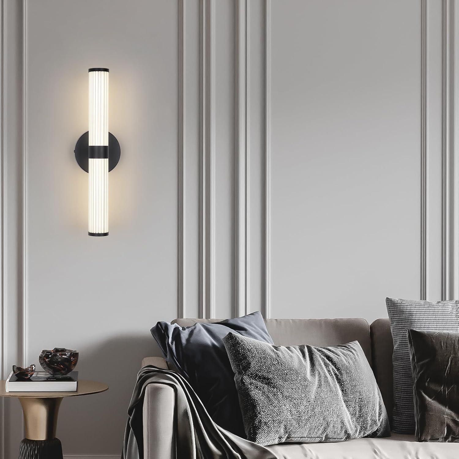 Modern wall sconce on a gray paneled wall with a sofa and decorative pillows in the foreground.