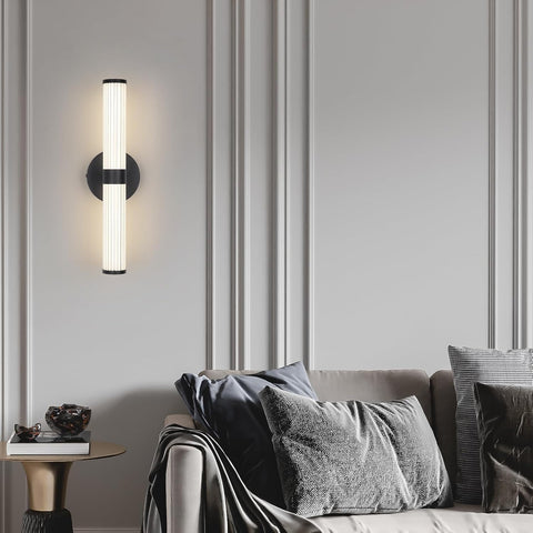 Modern wall sconce on a gray paneled wall with a sofa and decorative pillows in the foreground.
