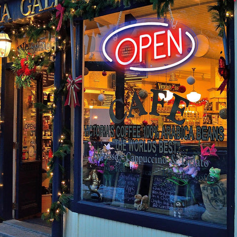 Neon 'OPEN' sign above a cafe window with Christmas decorations.
