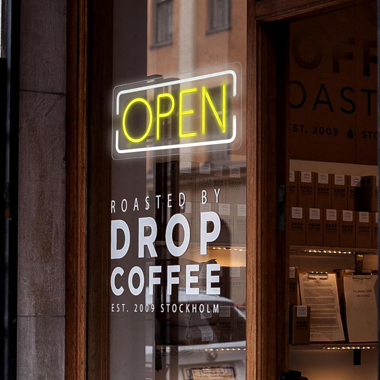 Neon 'OPEN' sign on a glass door of a coffee shop named 'Drop Coffee'.