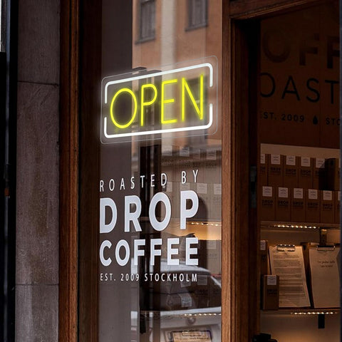 Neon 'OPEN' sign on a glass door of a coffee shop named 'Drop Coffee'.