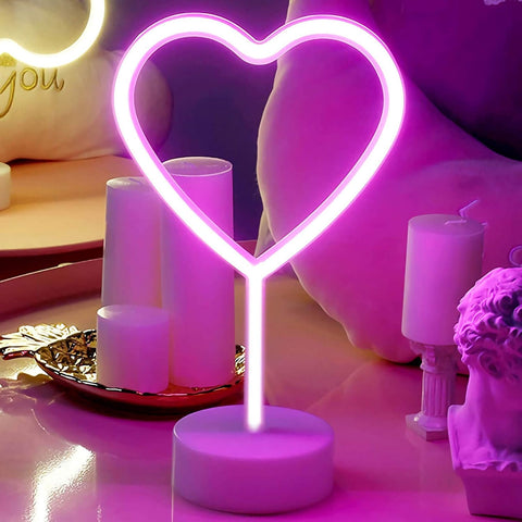 Neon heart-shaped light on a table with candles and decorative items.