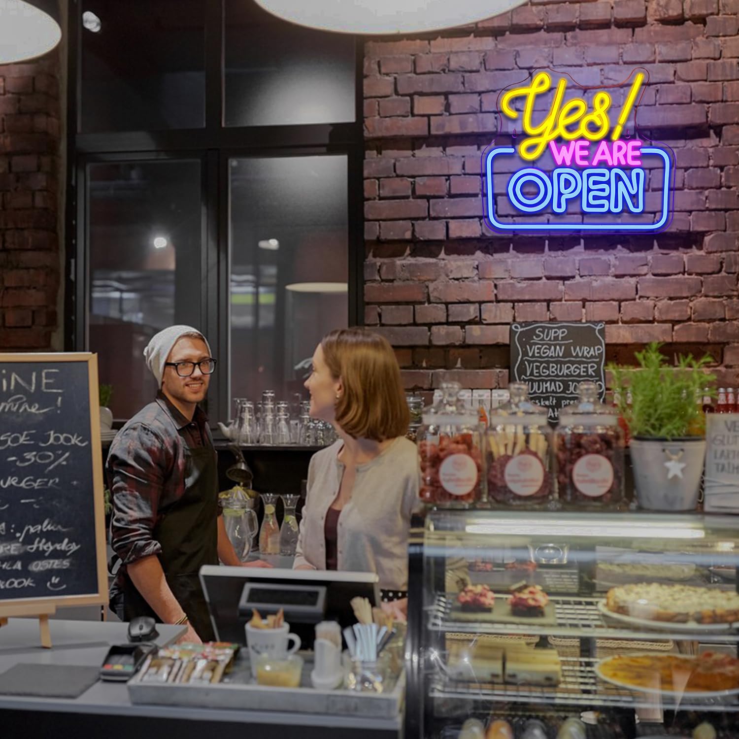 Neon sign 'Yes! We Are Open' above a counter with a customer and employee in a restaurant setting.