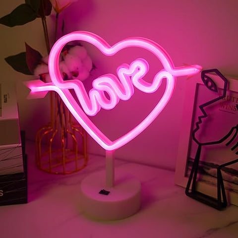 Neon sign shaped like a heart with the word 'love' inside, on a stand against a pink background.