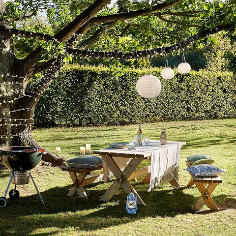 Outdoor setting with a table, chairs, and a grill under string lights and paper lanterns.