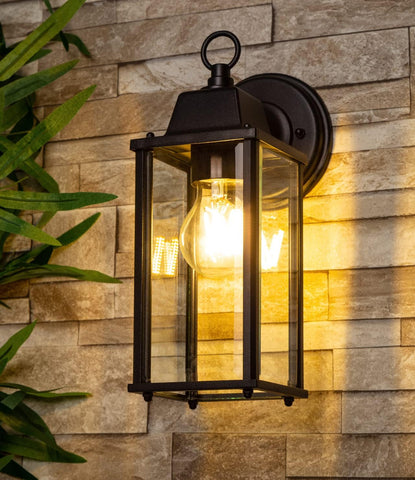 Outdoor wall light fixture on a stone wall with a plant to the left.