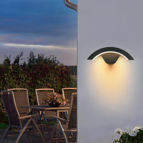 Outdoor wall light fixture on a white wall with a patio table and chairs in the background.
