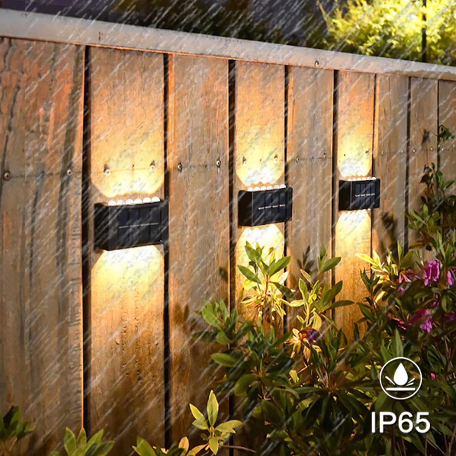 Outdoor wall lights on a wooden fence with plants and raindrops.