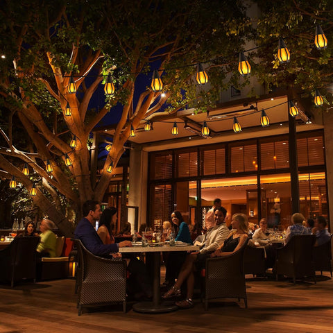 People dining outdoors at night with tree decorations and string lights.
