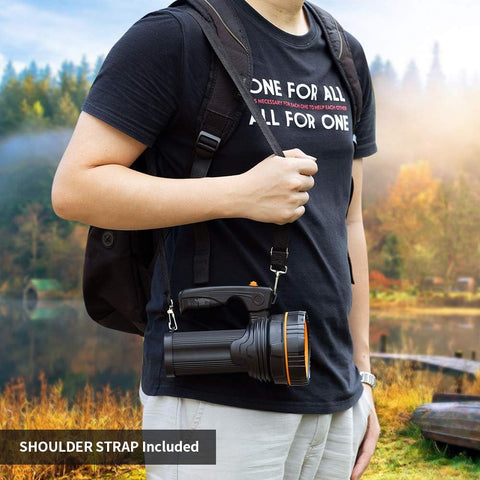 Person holding a flashlight with a shoulder strap, standing outdoors near a lake.