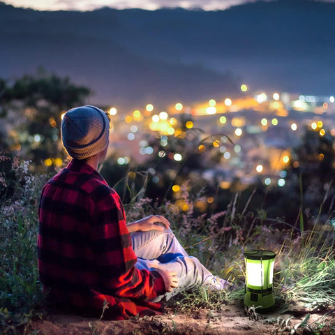 Person sitting by a lantern on a hill overlooking a cityscape at night