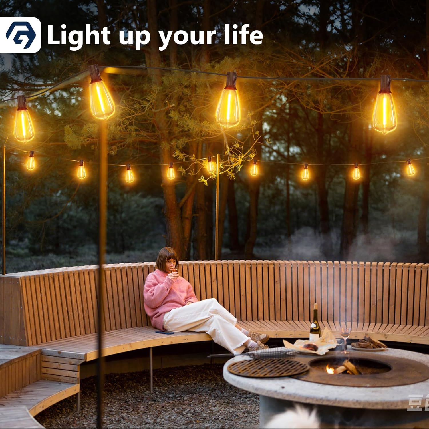 Person sitting on a wooden bench by a fire pit with string lights in a forest setting, featuring the text 'Light up your life'.