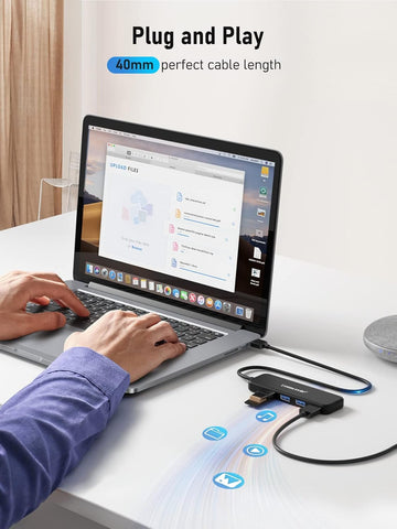 Person using a laptop with a USB hub on a desk, emphasizing 'Plug and Play' feature.