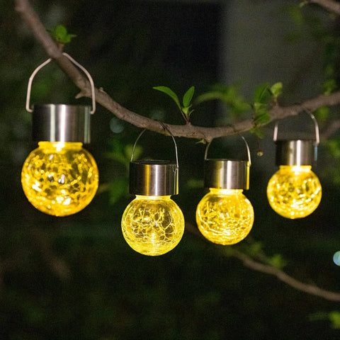 Solar string lights with yellow bulb lights hanging on a tree branch at night.