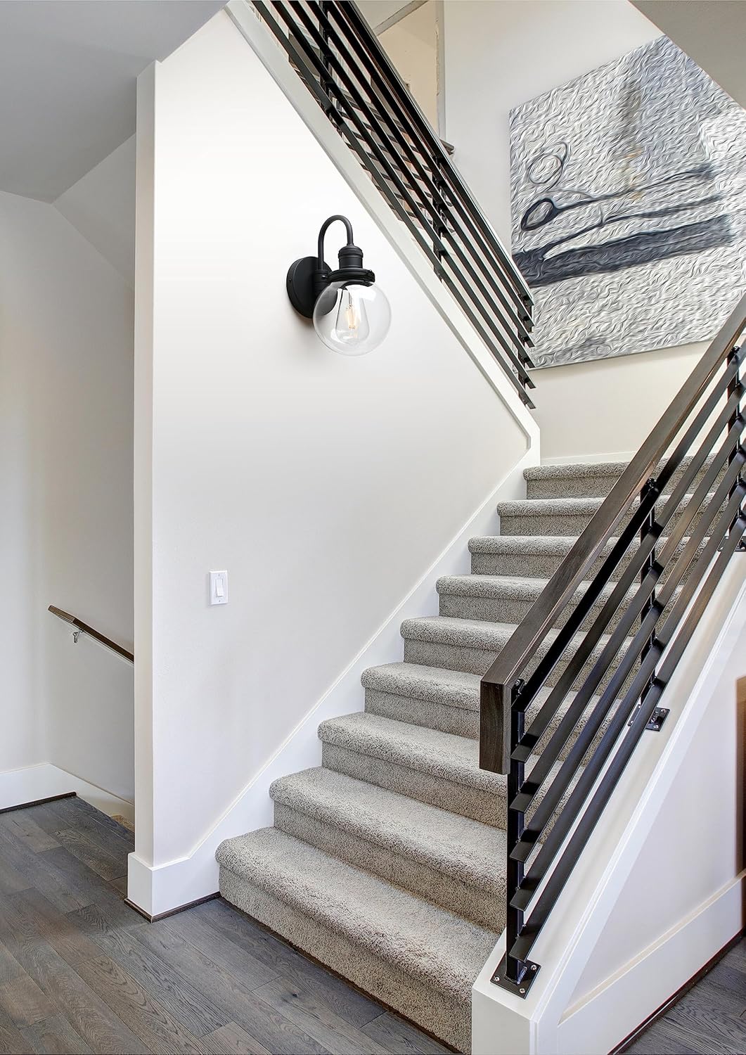 Staircase with carpeted steps and black metal railing, wall light fixture, and abstract painting.