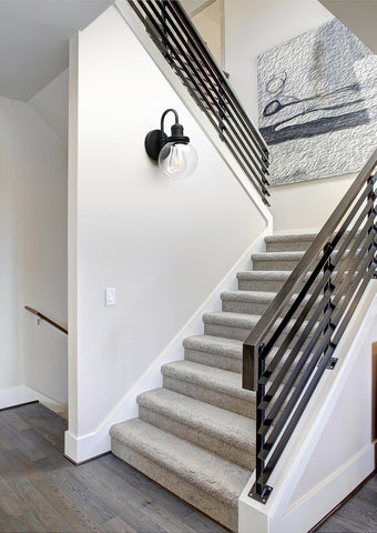 Staircase with carpeted steps and black metal railing, wall light fixture, and abstract painting.