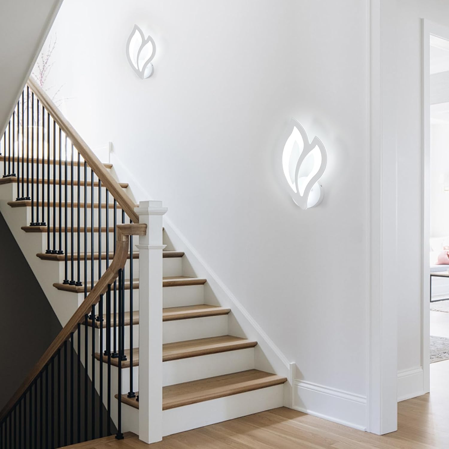 Staircase with wooden steps and black railings against a white wall with modern wall lights.
