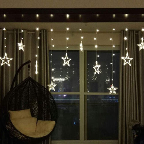 Star-shaped string lights hanging above a window with a dark curtain and a hanging chair.