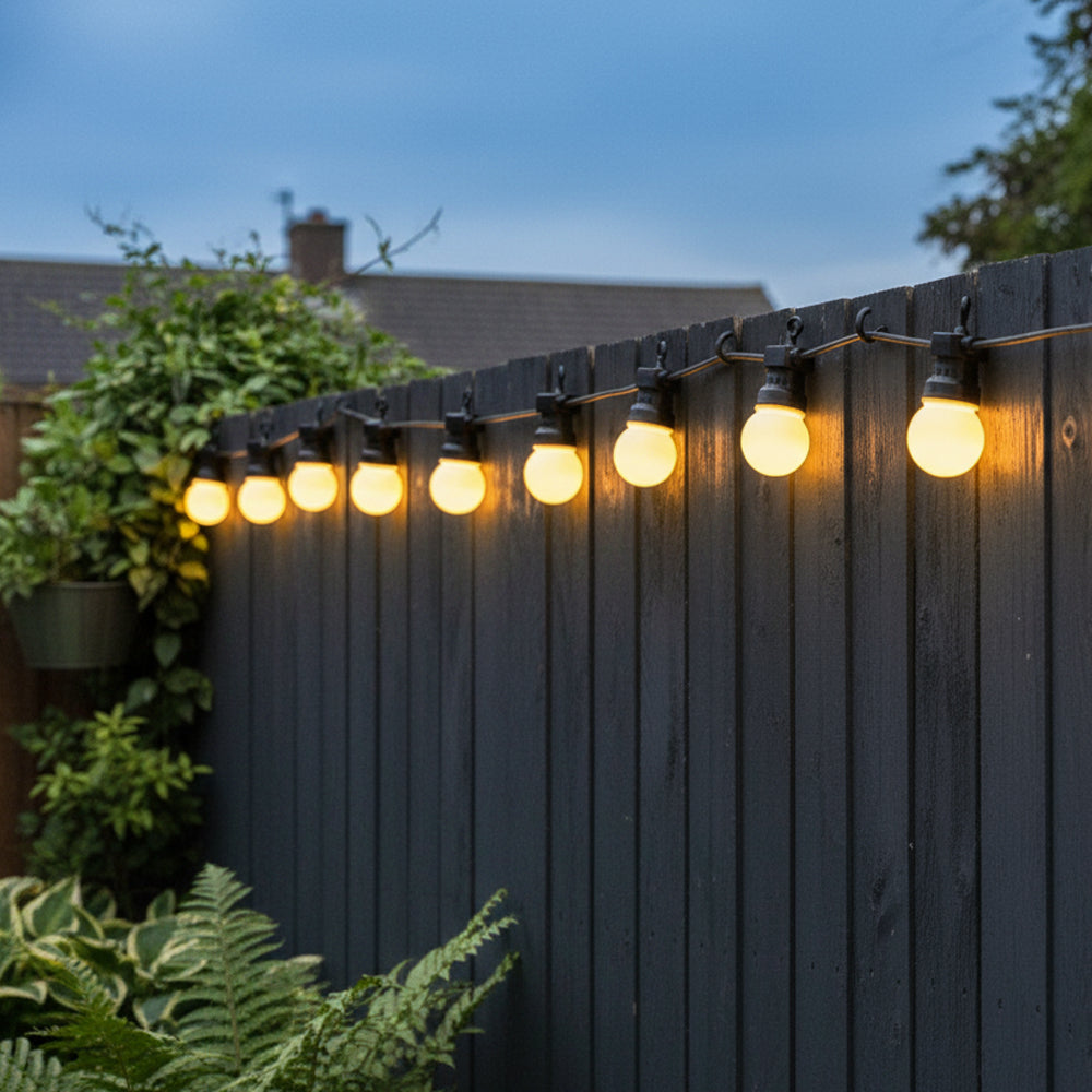 String lights on a wooden fence with plants and sky in the background