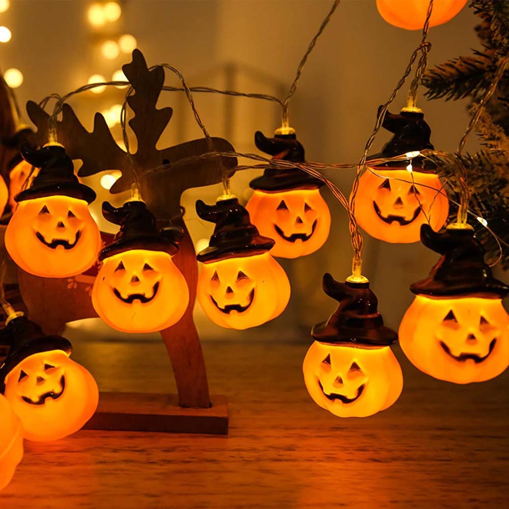 String lights with pumpkin and witch hat decorations on a wooden surface.