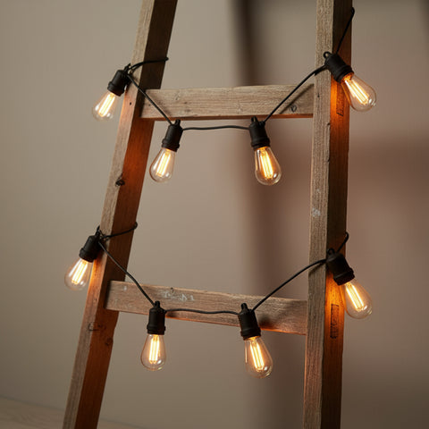 String of light bulbs hanging from a wooden ladder against a neutral background