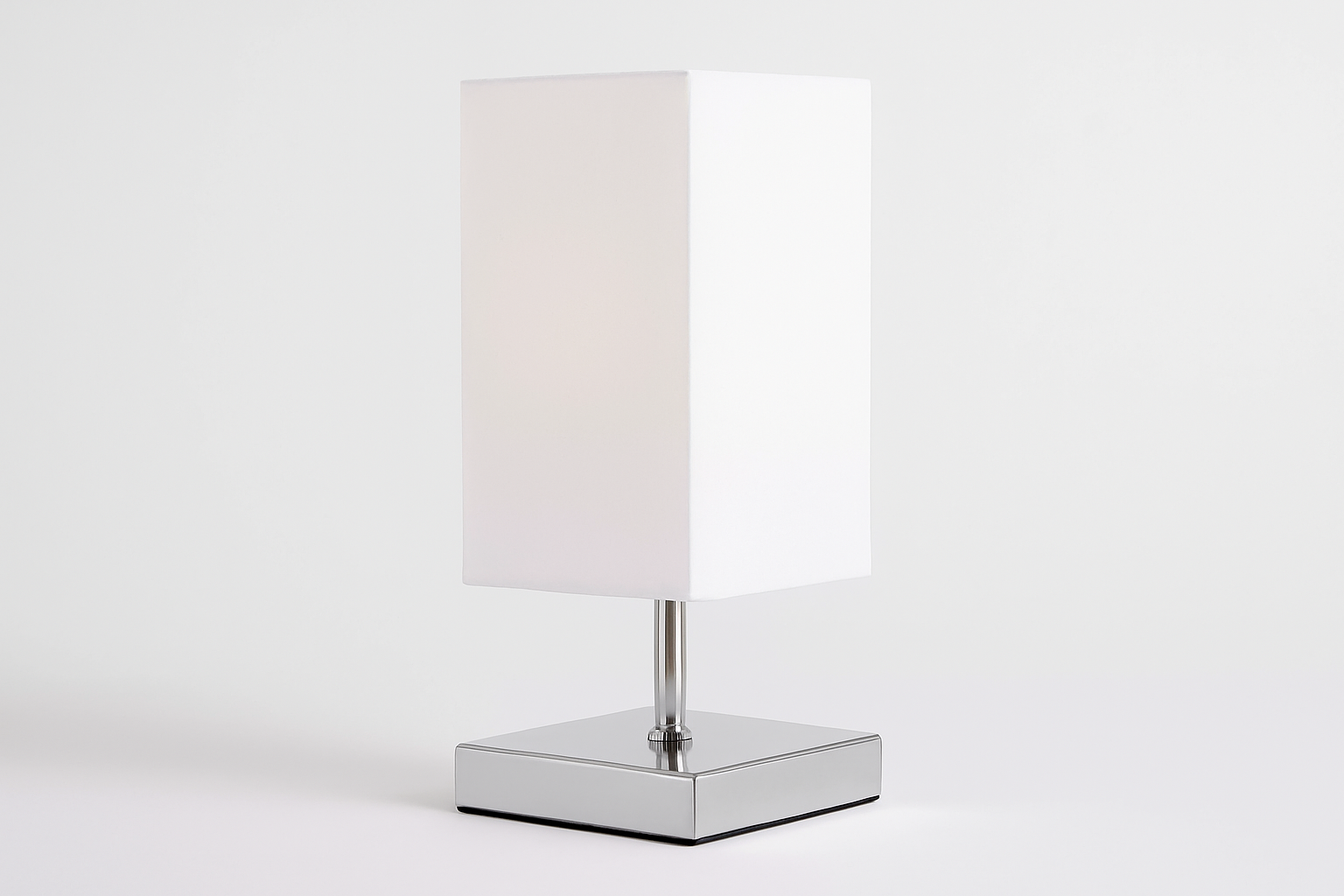 Table lamp with a white rectangular shade on a reflective base against a white background