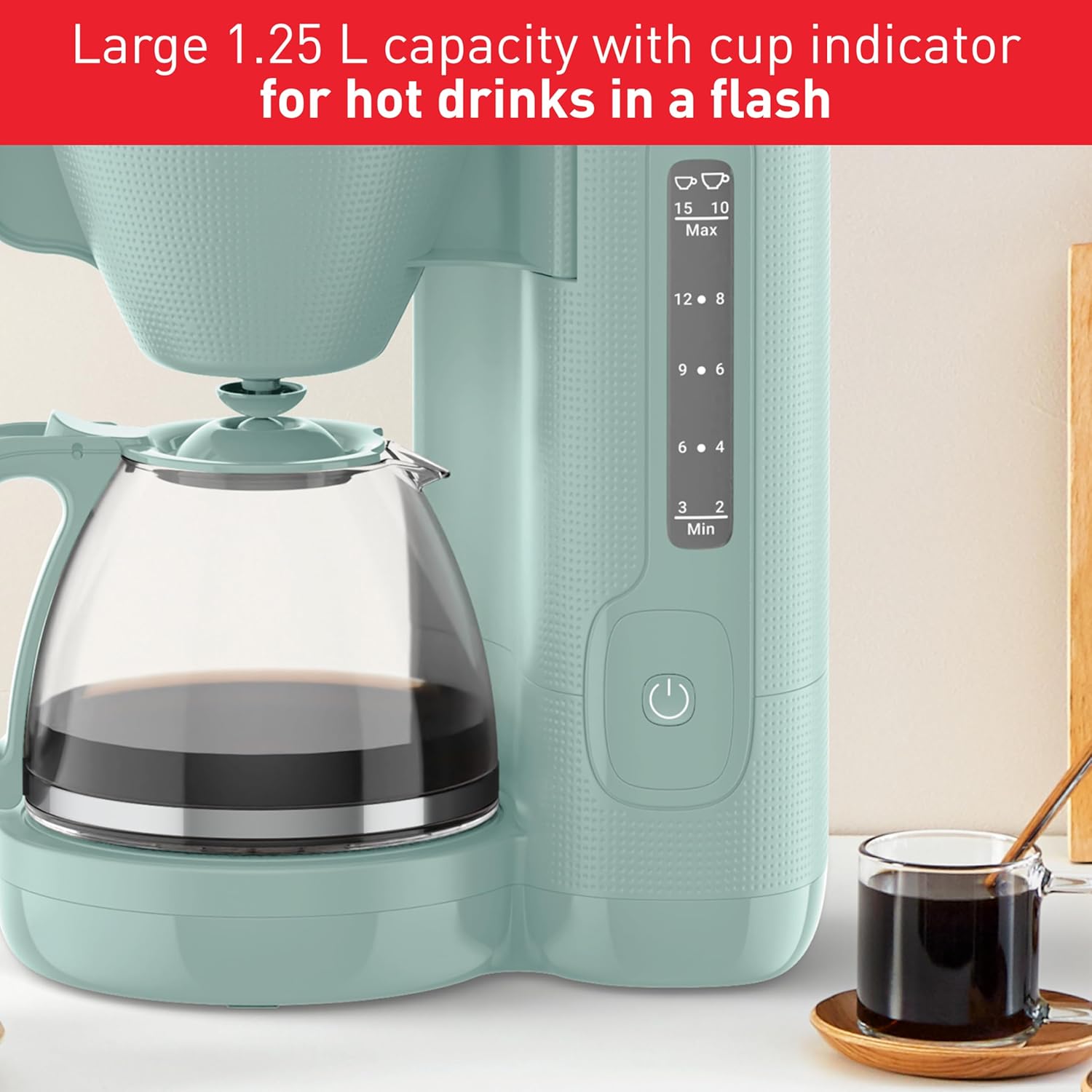 Teal coffee maker with glass carafe and cup of coffee on a white surface.