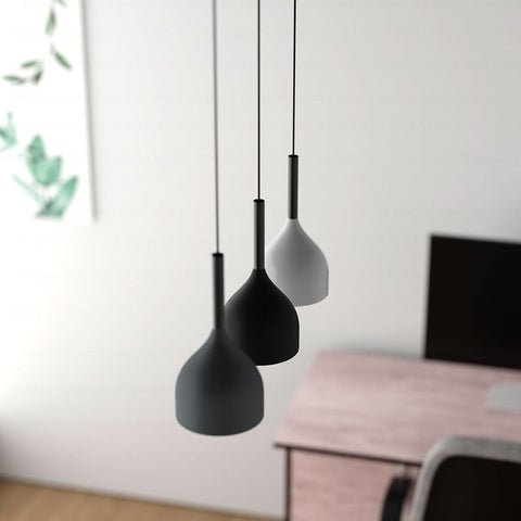 Three black pendant lights hanging against a white wall with a blurred background.