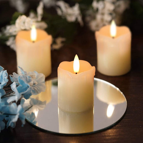 Three lit candles on a reflective surface with flowers in the background