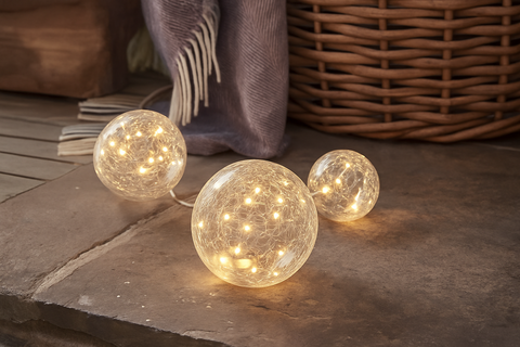 Three spherical string lights on a stone surface with a woven basket and fabric in the background.