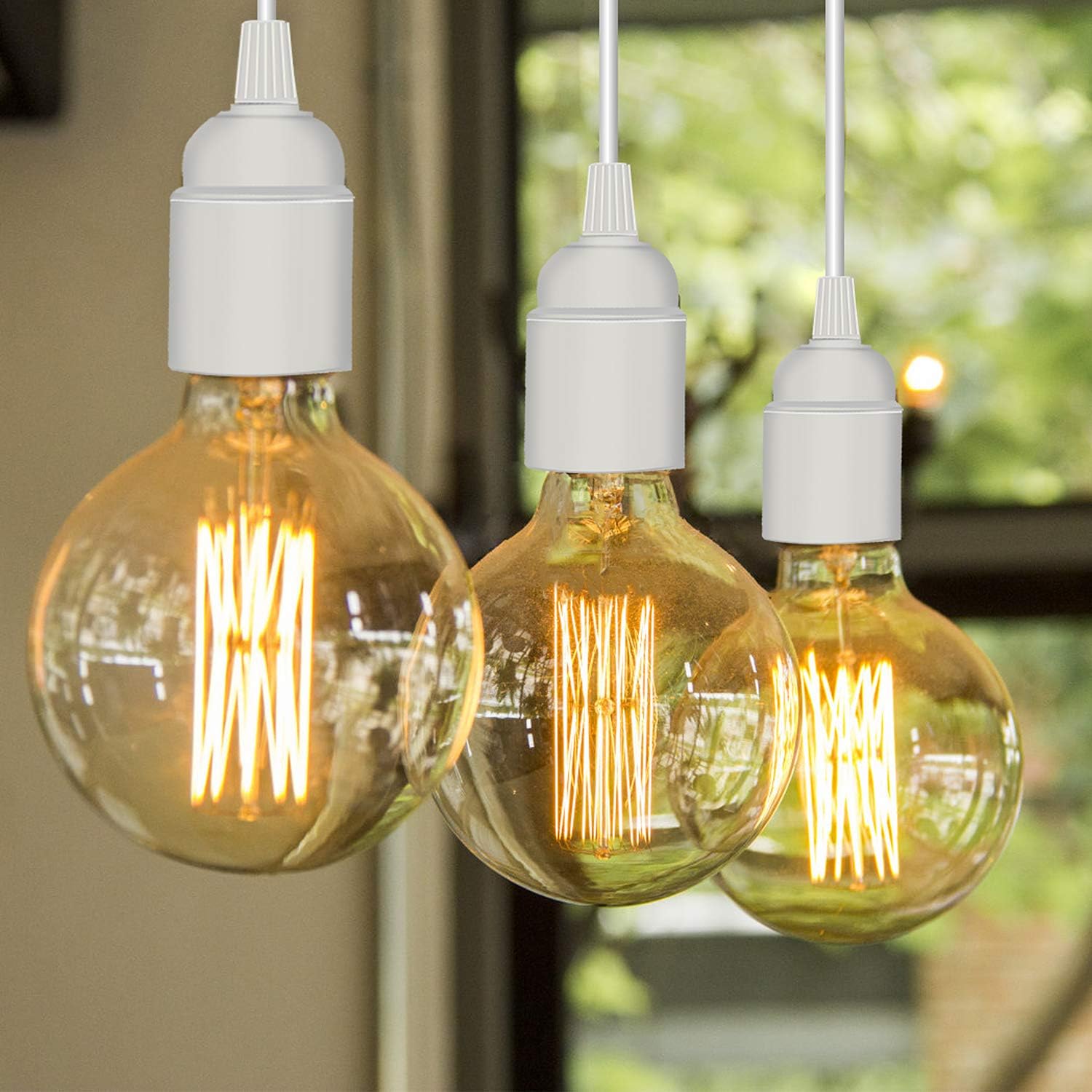 Three vintage-style light bulbs hanging in front of a blurred green outdoor background