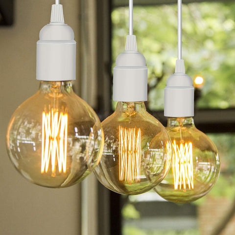 Three vintage-style light bulbs hanging in front of a blurred green outdoor background
