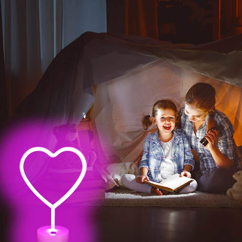 Two children sitting under a blanket fort, reading a book with a heart-shaped night light in the foreground.