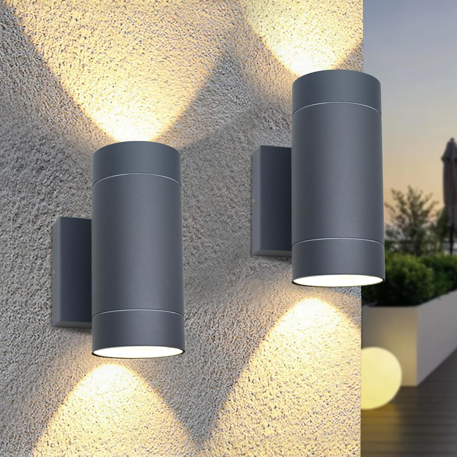 Two cylindrical outdoor wall lights on a textured stone wall with a blurred garden background.