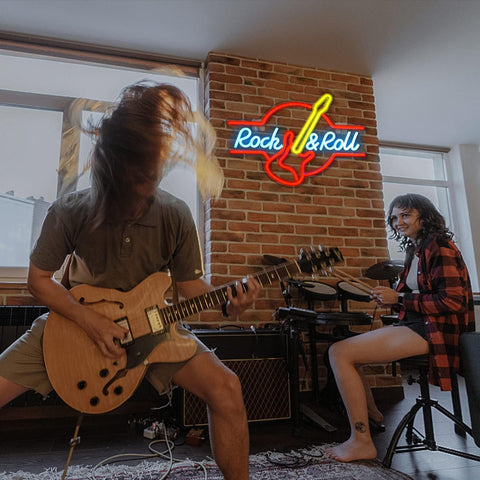 Two musicians playing guitar and drums in a room with a 'Rock & Roll' neon sign.