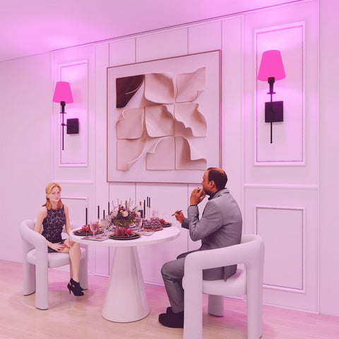 Two people sitting at a table in a stylish room with pink lighting.