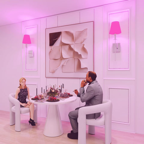 Two people sitting at a table in a stylish room with pink lighting.