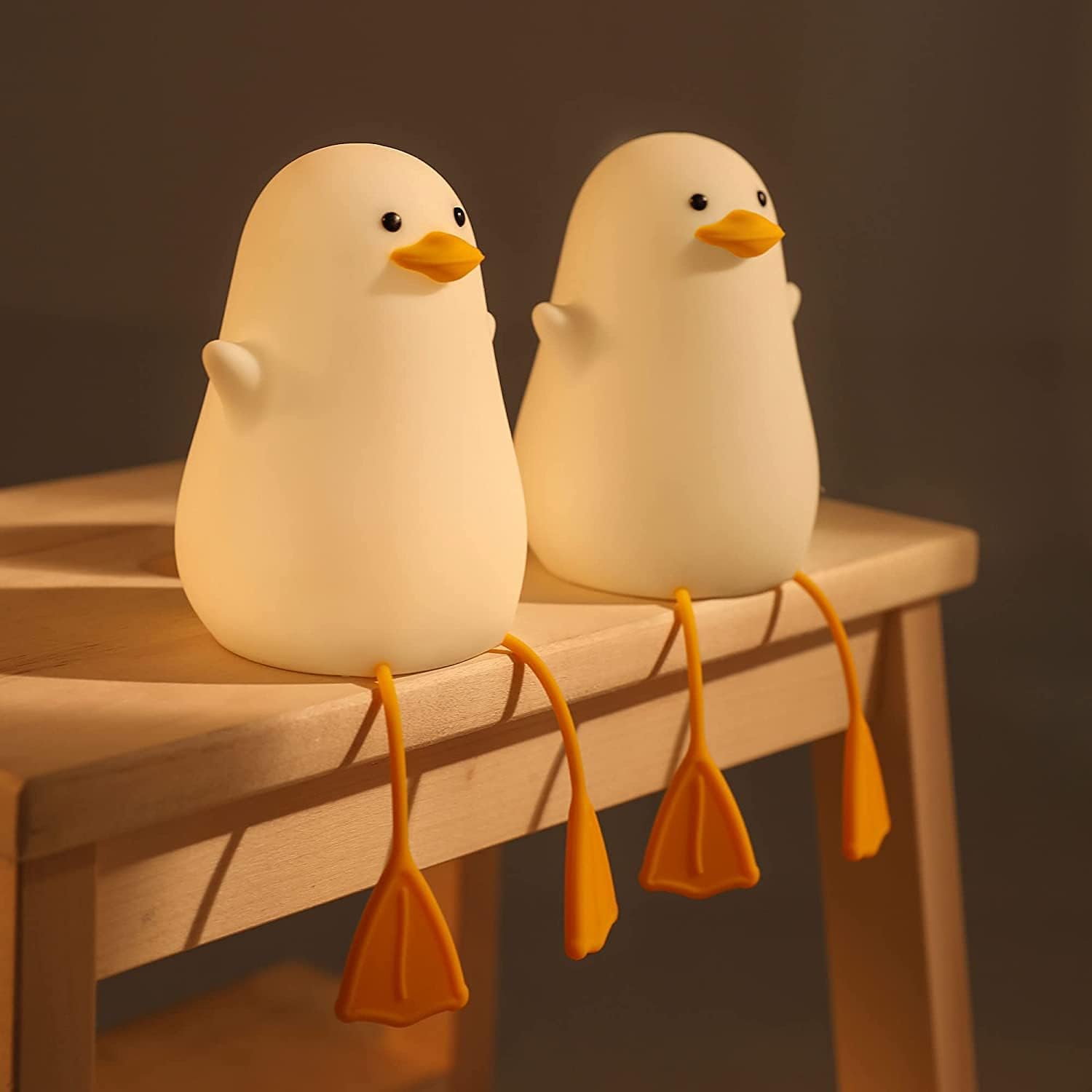 Two white duck-shaped lamps with orange beaks and feet on a wooden surface.
