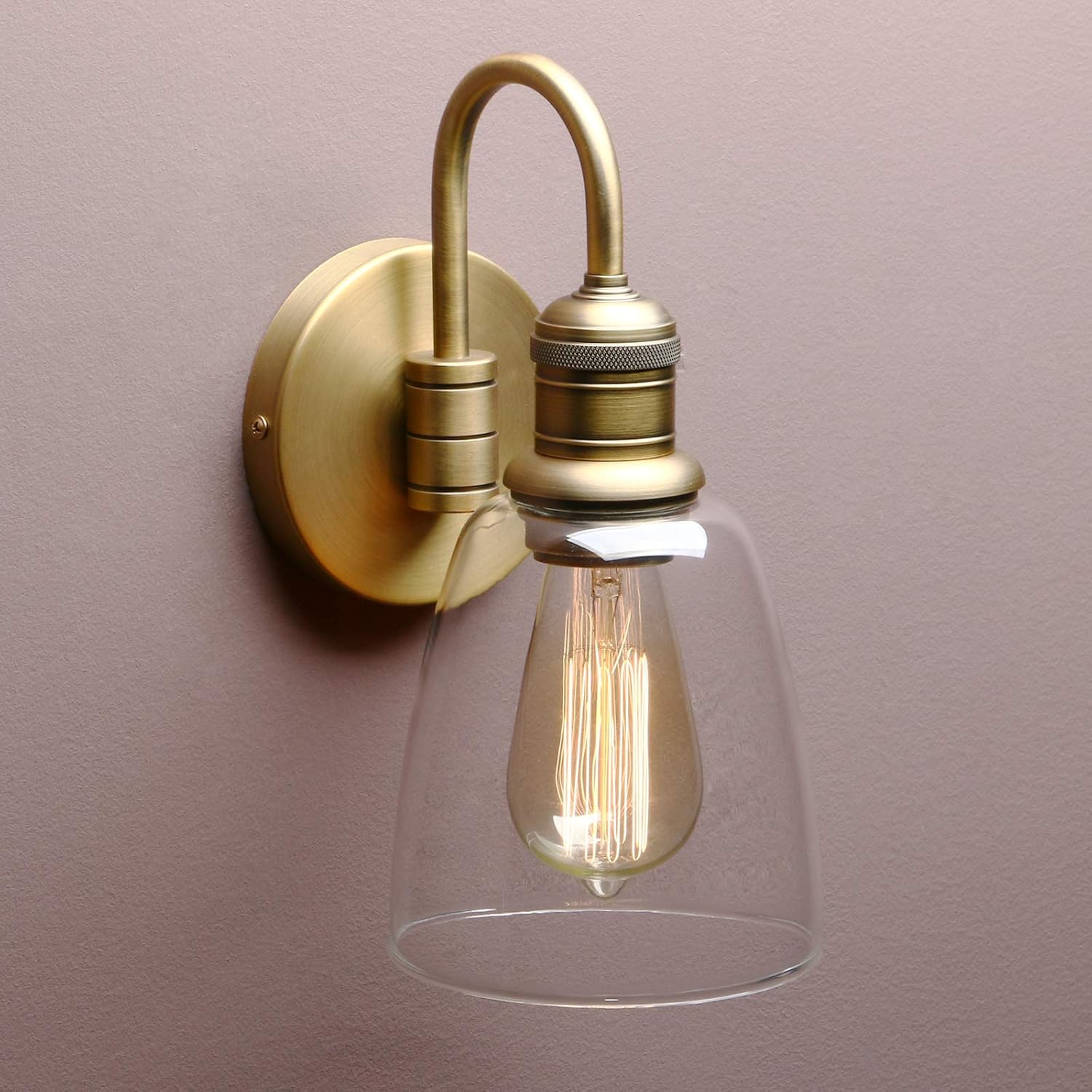 Vintage-style wall light fixture with clear glass shade and brass finish on a plain background