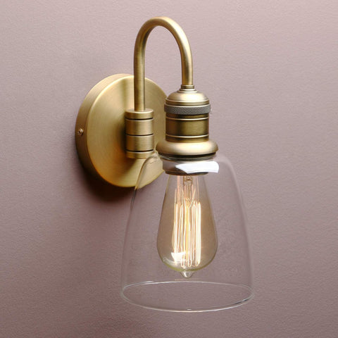Vintage-style wall light fixture with clear glass shade and brass finish on a plain background