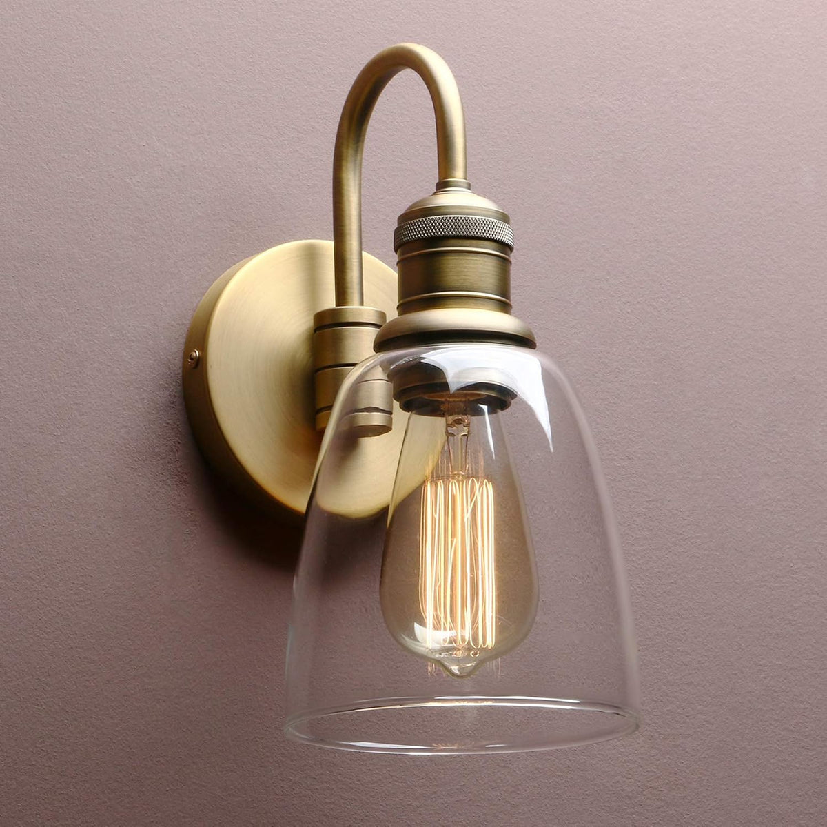 Vintage-style wall sconce with clear glass shade and brass fixture on a plain background