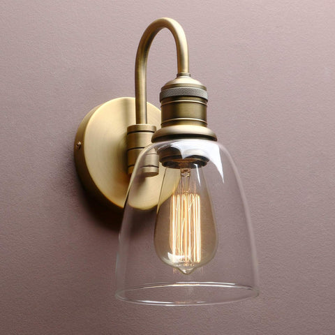 Vintage-style wall sconce with clear glass shade and brass fixture on a plain background